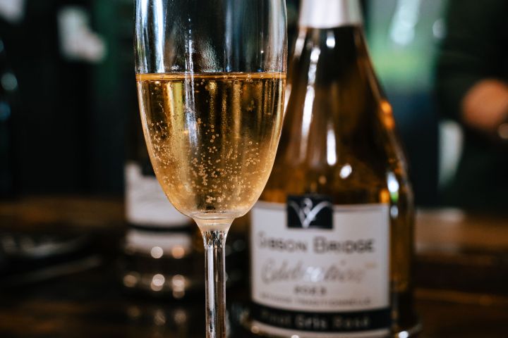 Champagne flute with bubbly drink, bottle in background on wooden table.