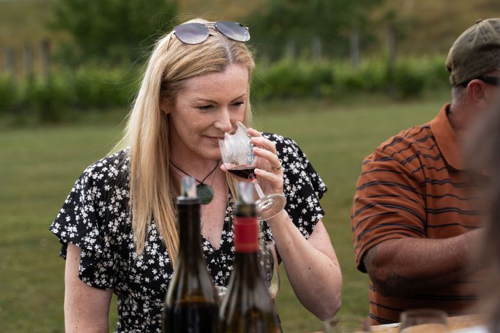 Woman smelling red wine at an outdoor table with wine bottles.