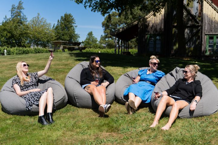 Four women relaxing on bean bags outdoors with drinks, under a tree.