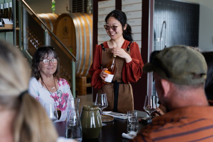 Woman presenting wine to seated guests at a winery tasting event.