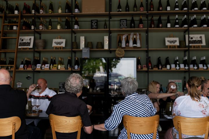 People in a wine bar with bottles on shelves and a ladder.