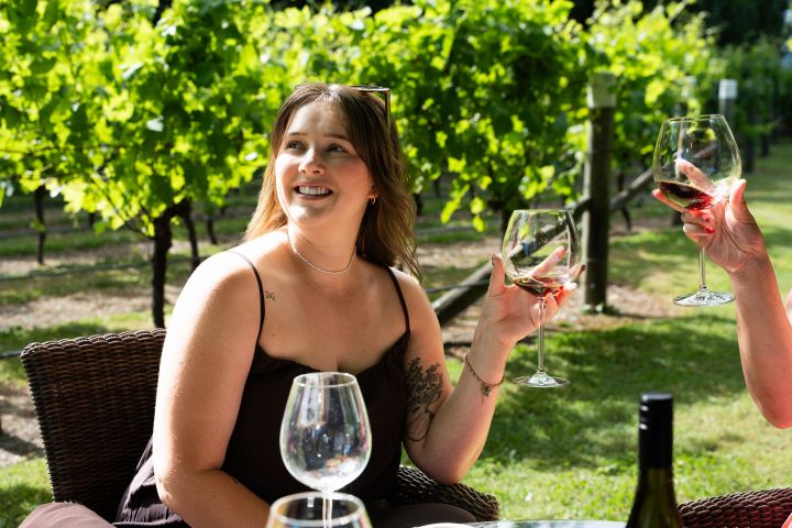 Woman sitting at vineyard table, holding a glass of wine and smiling.